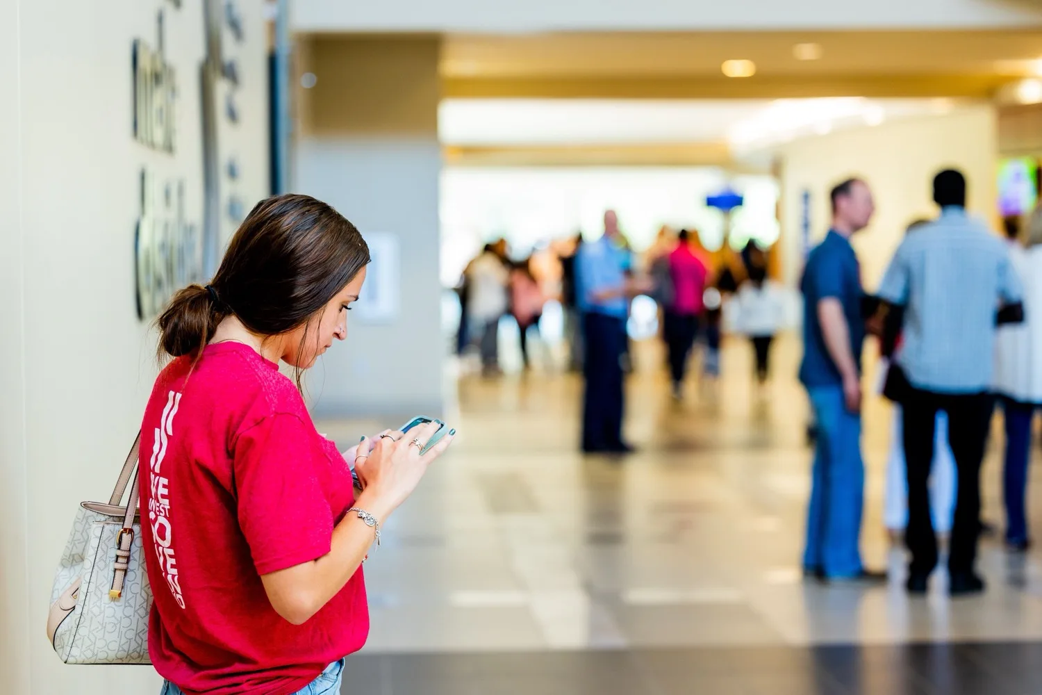 A shopper typing on her phone in a busy, crowded mall corridor, the kind of rushed, divided attention that BFCM's mobile checkout friction runs into at scale